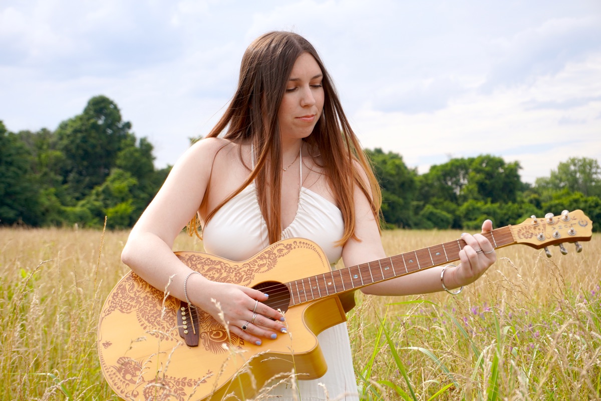 Cara Paige playing guitar in a field