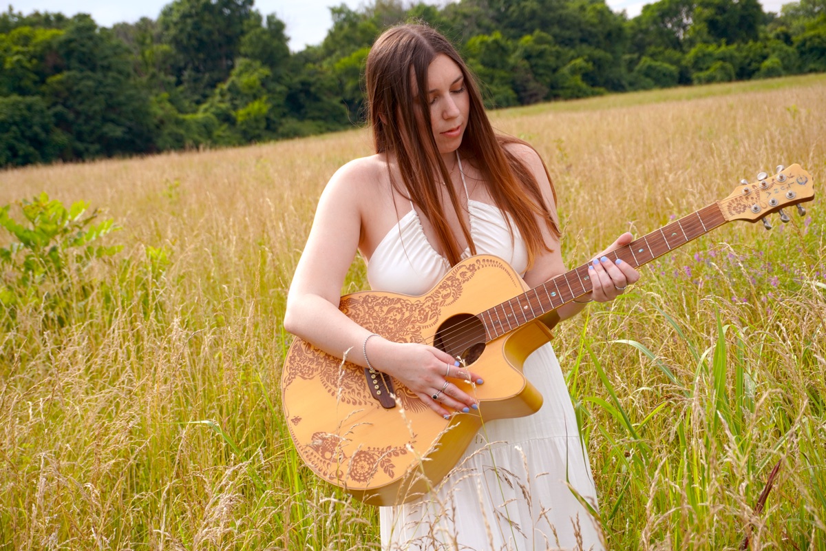 Cara Paige playing guitar in a golden field